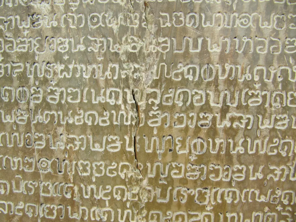 Ancient manuscript with inscribed Thai script characters, showing the long tradition of written Thai as an abugida with consonant-class tone system